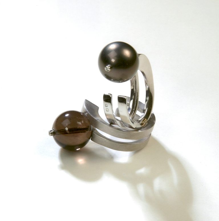 Stylish modern ring featuring silver bands and two decorative pearls in dark shades, showcasing contemporary jewelry design.