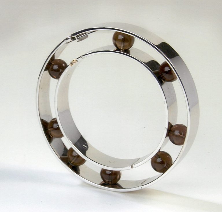 A modern silver ring featuring a circular design with brown beads embedded around its edge, showcasing a contemporary aesthetic.