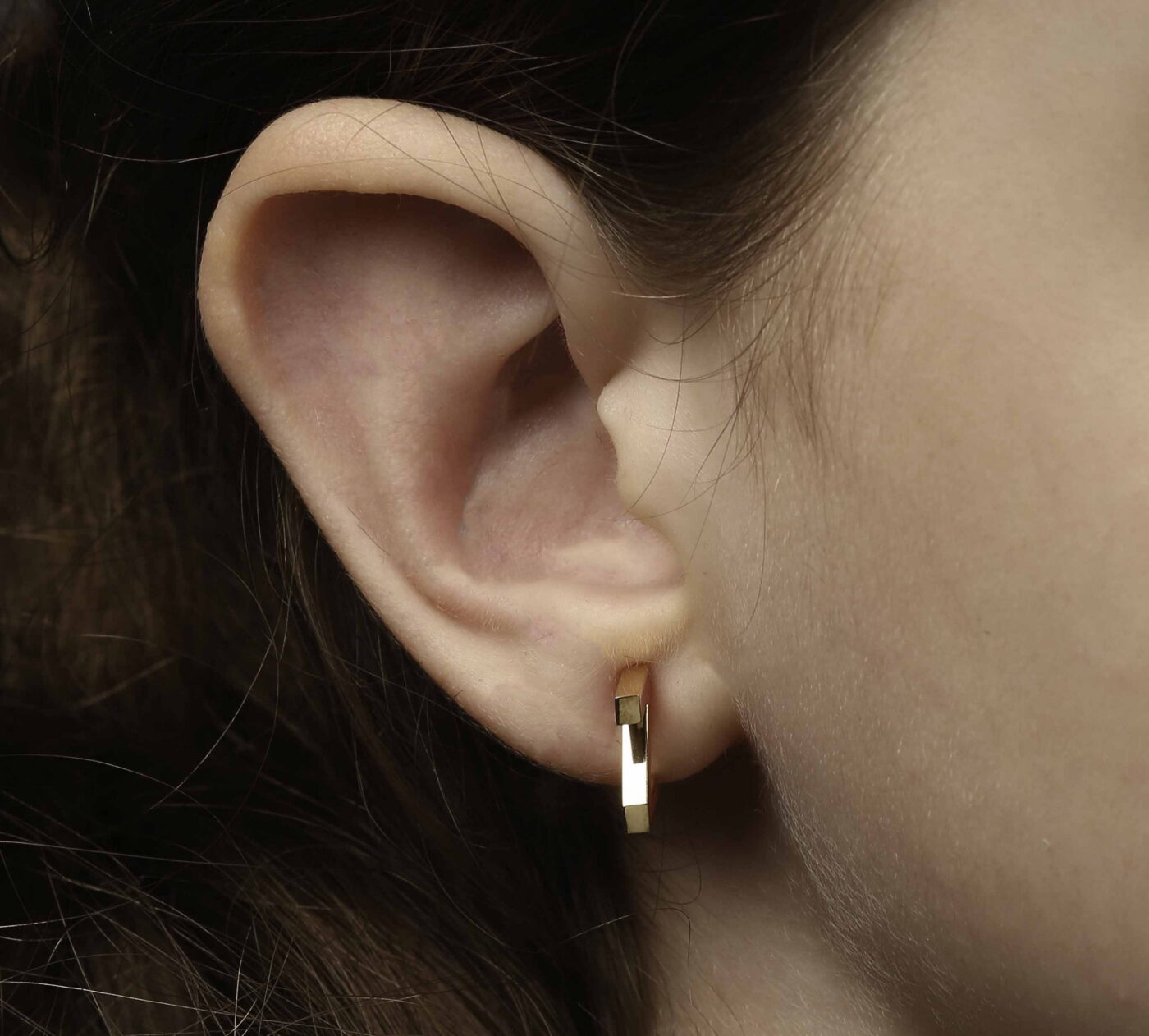 Close-up of a model's ear wearing gold hoop earrings, showcasing a modern and elegant design suitable for various occasions.