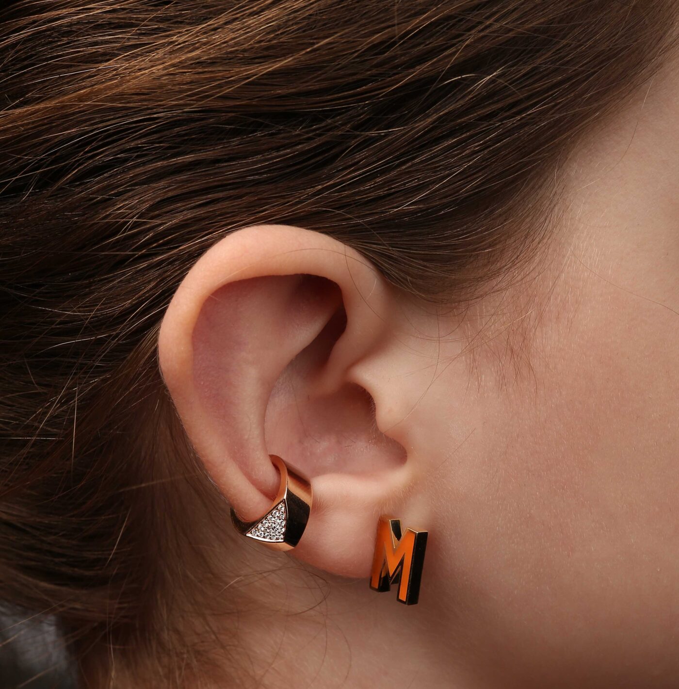 Gold and silver earrings on a model's ear showcasing modern design and elegance, featuring a geometric shape and sparkling accents.