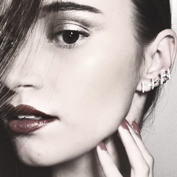 Close-up of a model showcasing elegant earrings and bold makeup, featuring red lips and manicured nails, highlighting contemporary fashion trends.