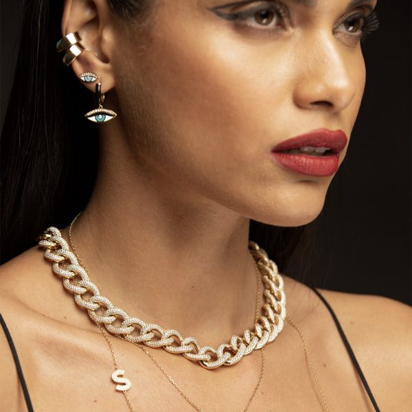 Close-up of a model showcasing gold jewelry including a chunky chain necklace and eye motif earrings and rings.