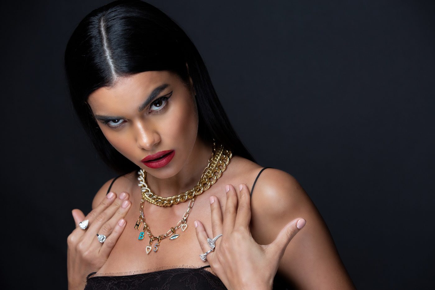 Model showcasing a variety of elegant jewelry including necklaces, rings, and bracelets against a dark background.