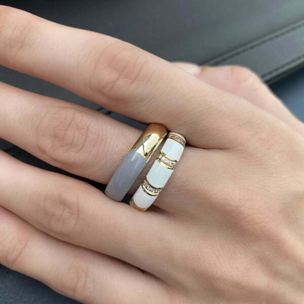 Close-up of three stylish rings on a hand, featuring a gold band, a gray band, and a white band with decorative elements.