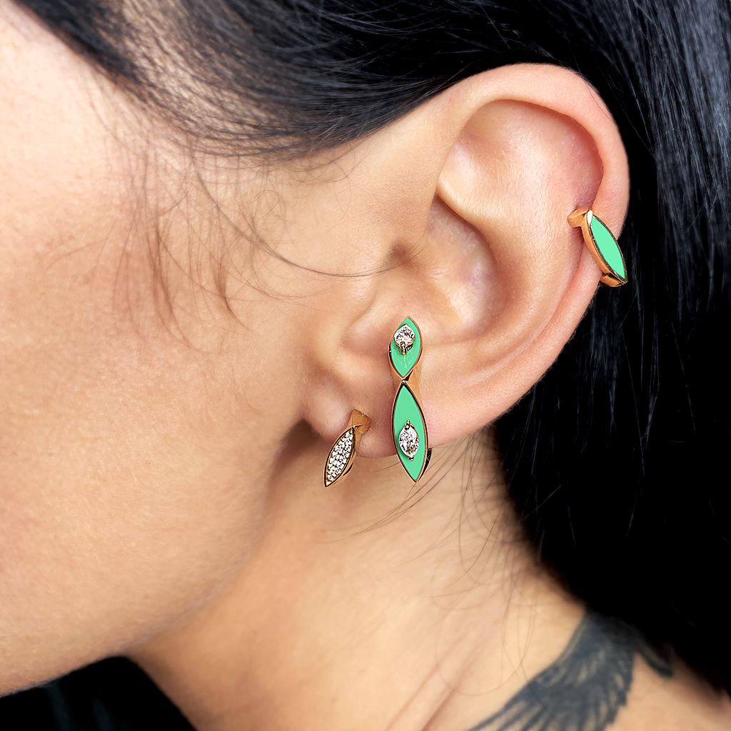 Close-up of earrings featuring green enamel and gold accents worn on a person's ear.