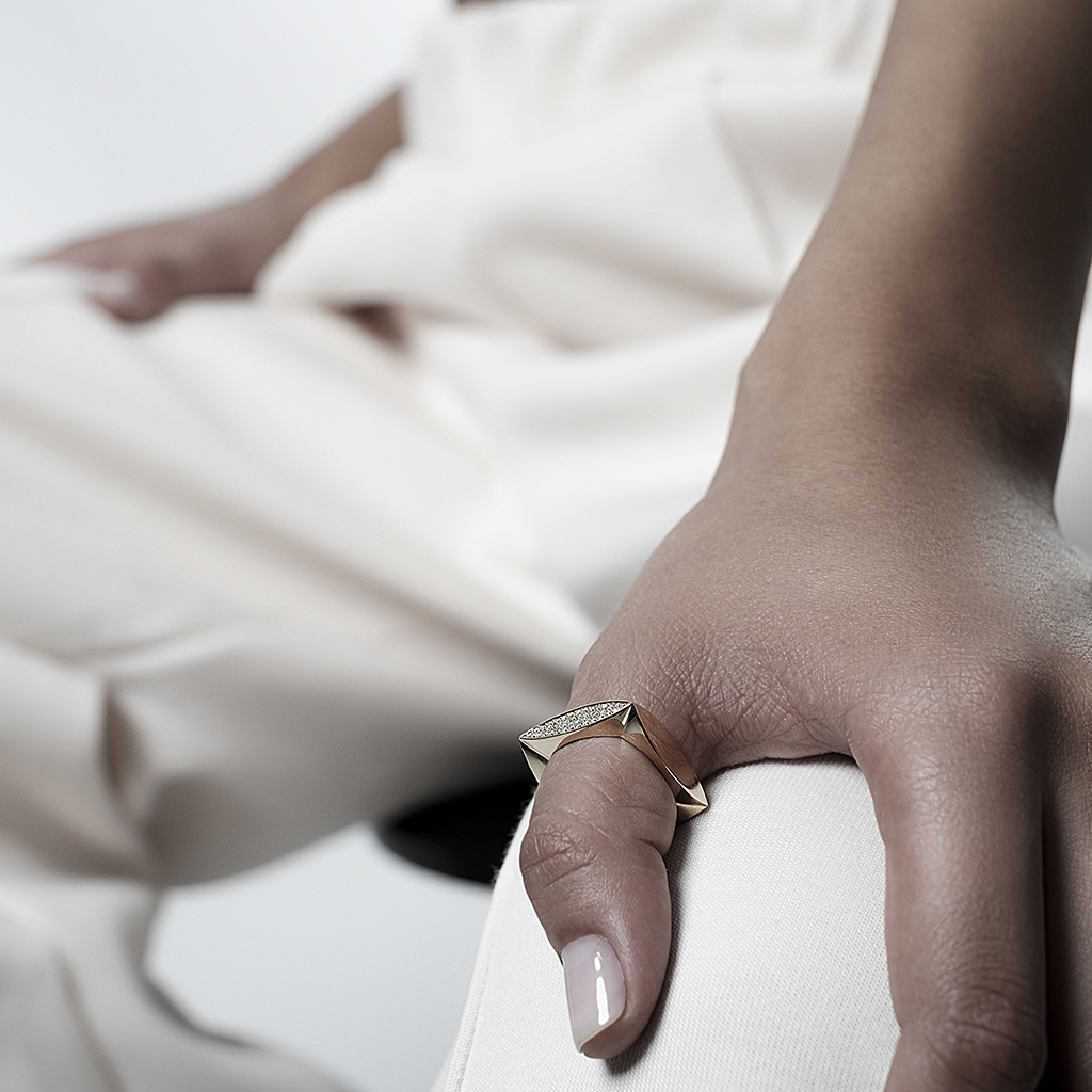 A hand wearing a gold geometric ring with a textured surface, resting on a leg.