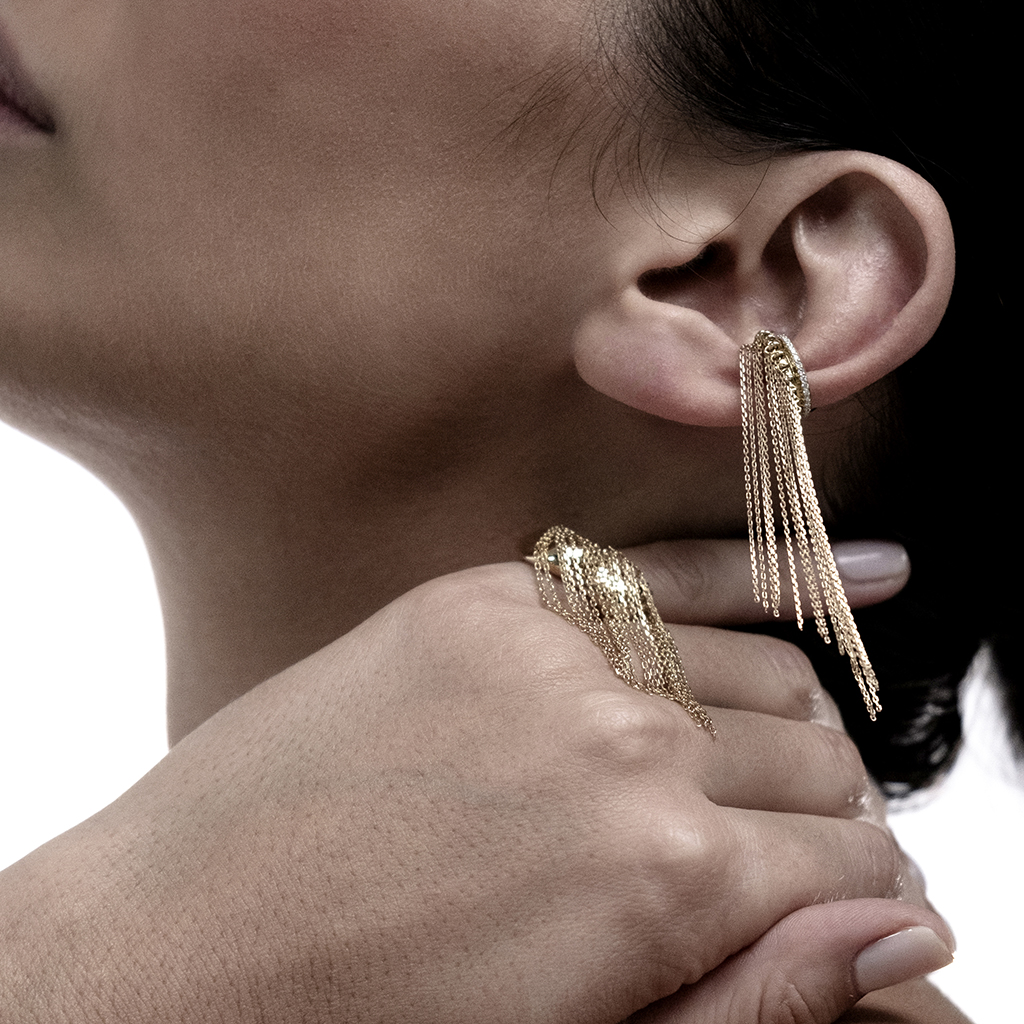 Model wearing gold chain earrings and a matching ring on her hand.