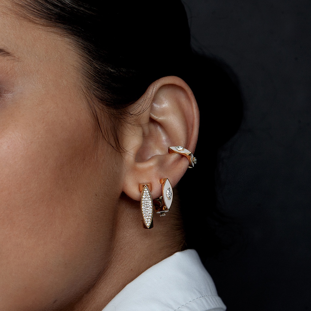 Close-up of a woman's ear adorned with elegant gold earrings featuring diamonds, showcasing modern jewelry design.