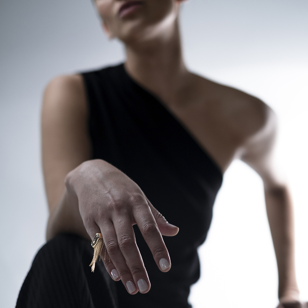 Close-up of a woman's hand adorned with a stylish gold ring, showcasing modern jewelry design against a neutral background.