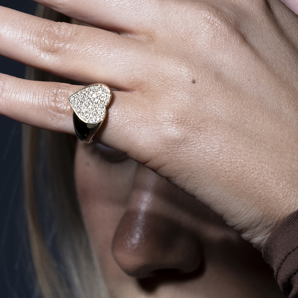 A hand wearing a gold and silver heart-shaped ring with a sparkling surface.