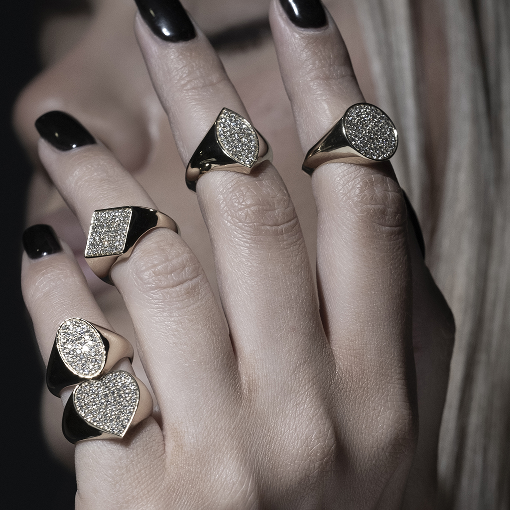 Five gold rings with sparkling surfaces worn on a hand with dark nails.