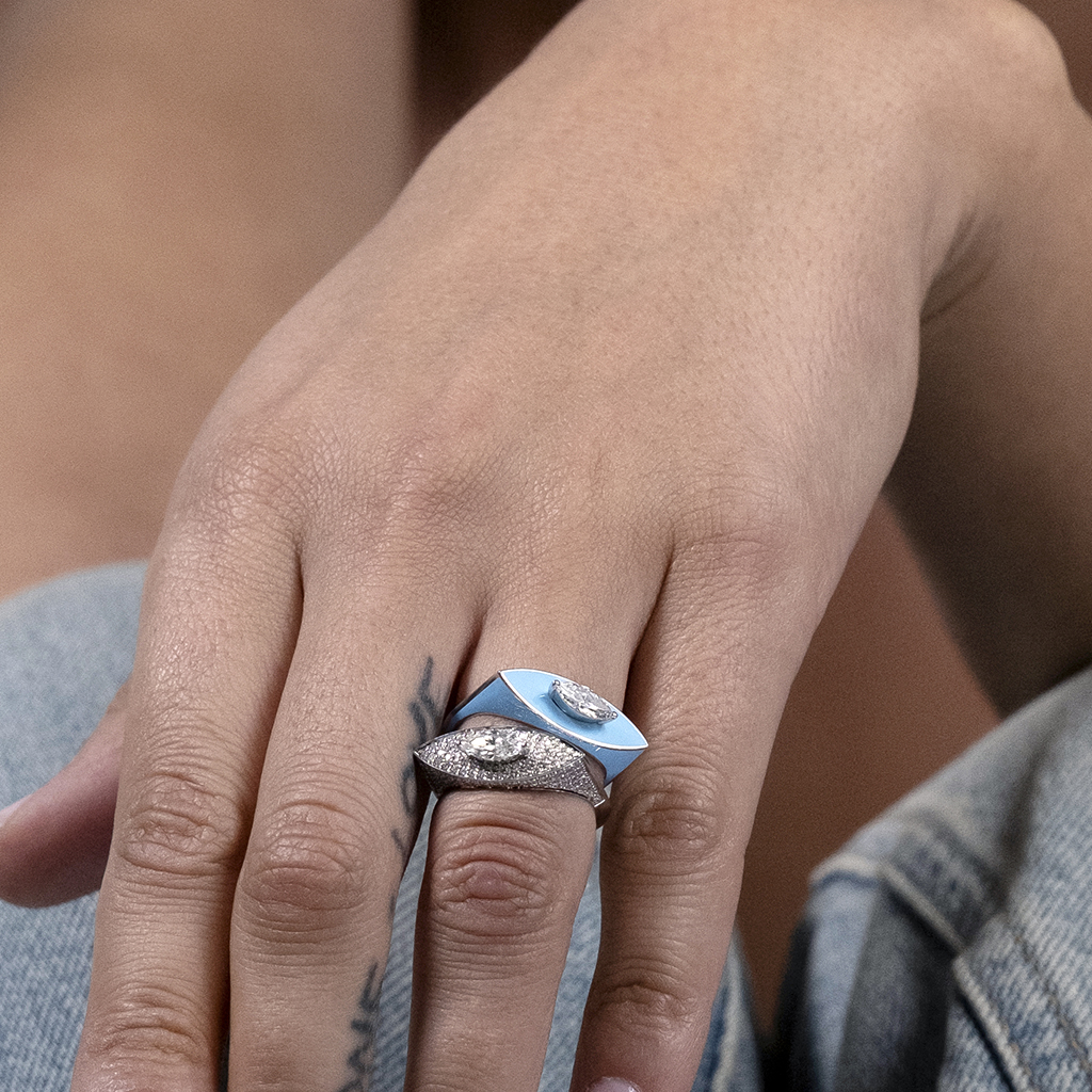 A hand displaying two rings, one silver with a textured design and one blue with a smooth finish, showcasing modern jewelry styles.