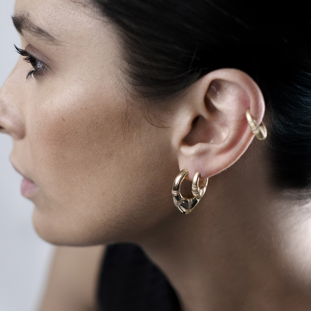 Close-up of a model wearing gold hoop earrings with a unique design.