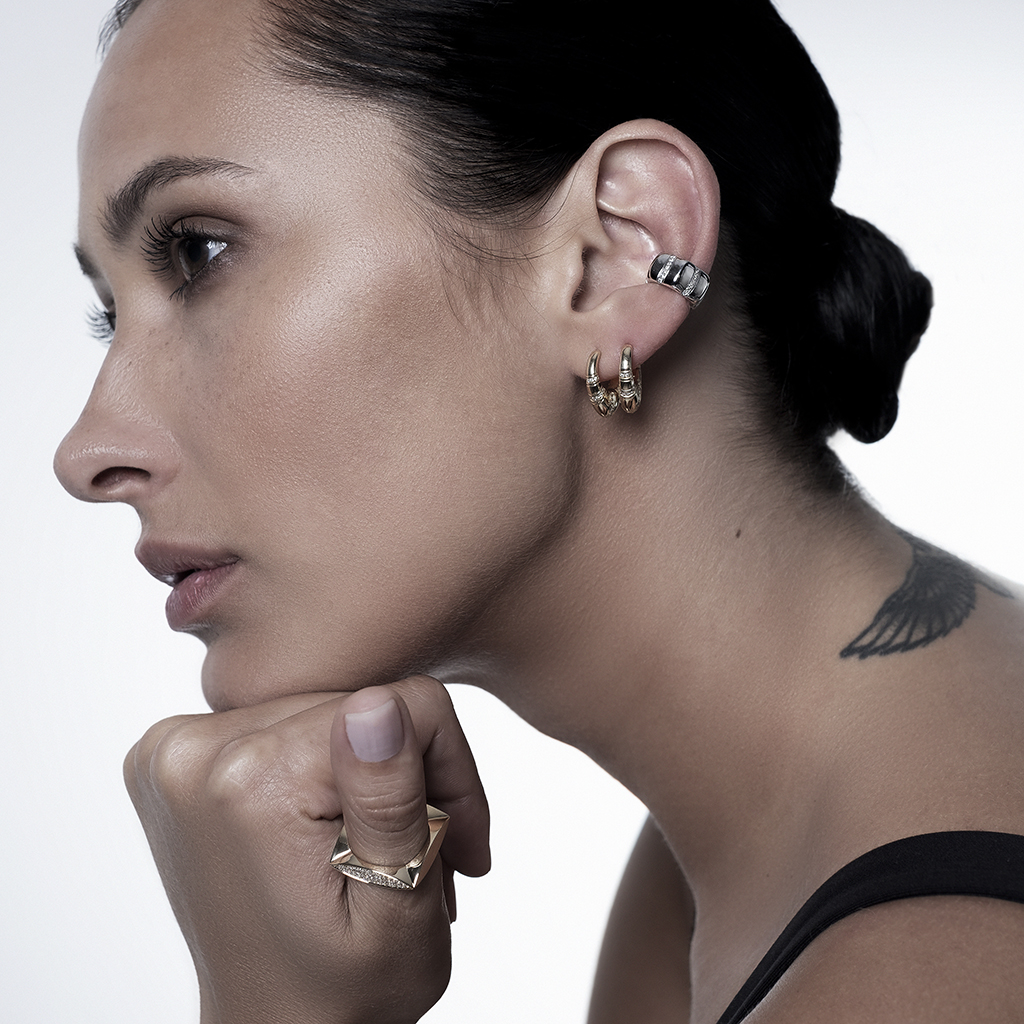 Profile view of a woman with a thoughtful expression, wearing gold and silver earrings and a ring.