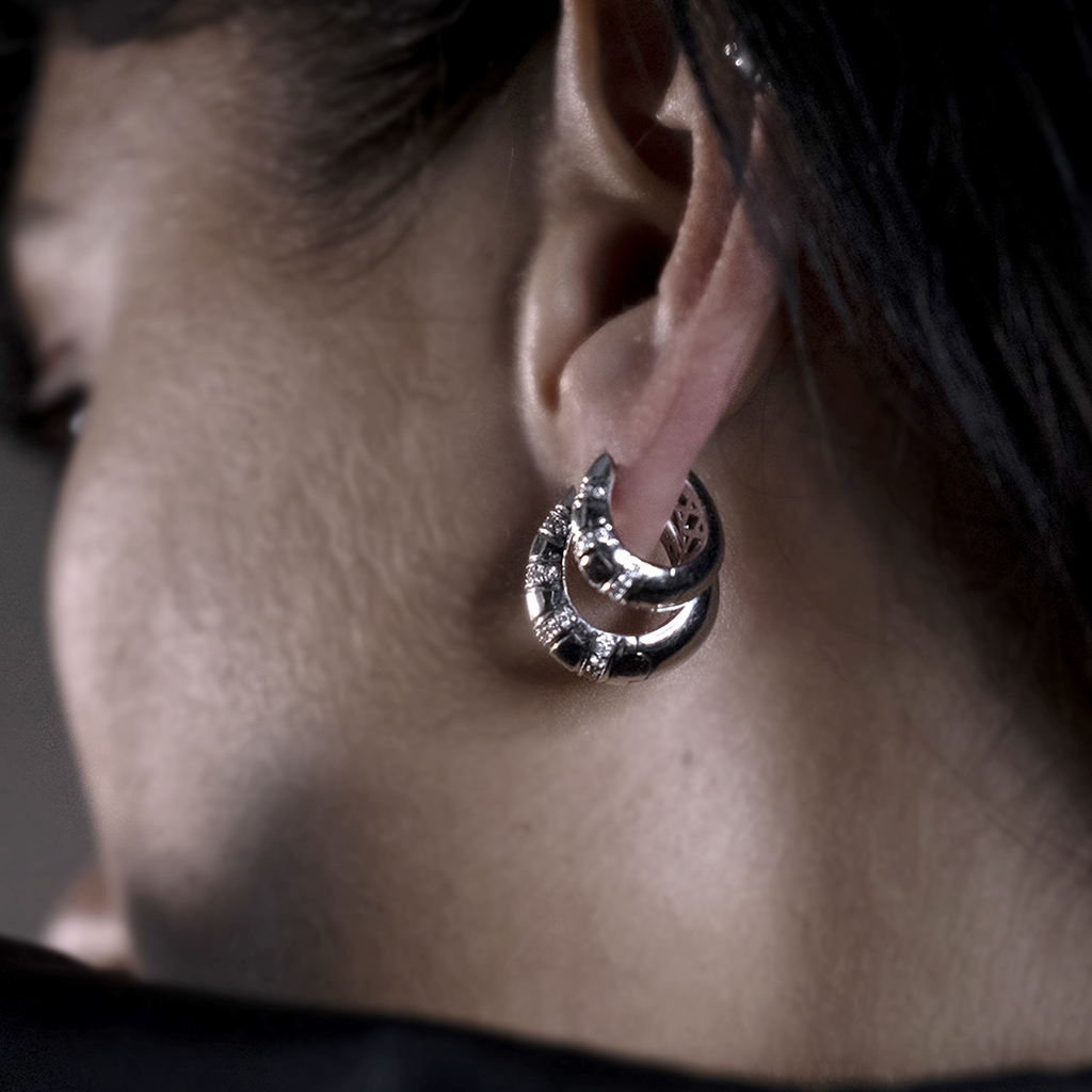 Close-up of a person wearing silver hoop earrings with intricate designs and embellishments.