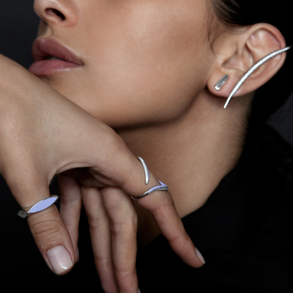 Close-up of a model's hand and ear adorned with silver jewelry, including rings and earrings.