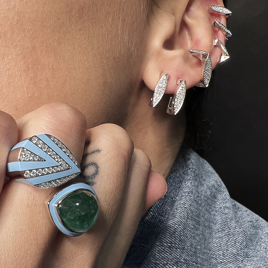 Close-up of a hand wearing a blue and silver ring with a green stone and multiple silver ear cuffs.