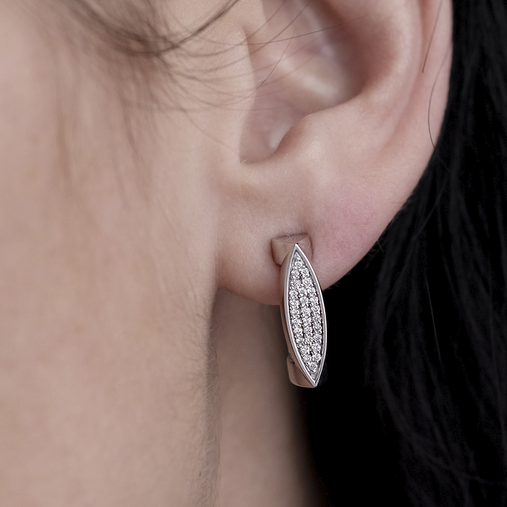 Close-up of a person's ear wearing silver earrings with diamond accents in a marquise shape.
