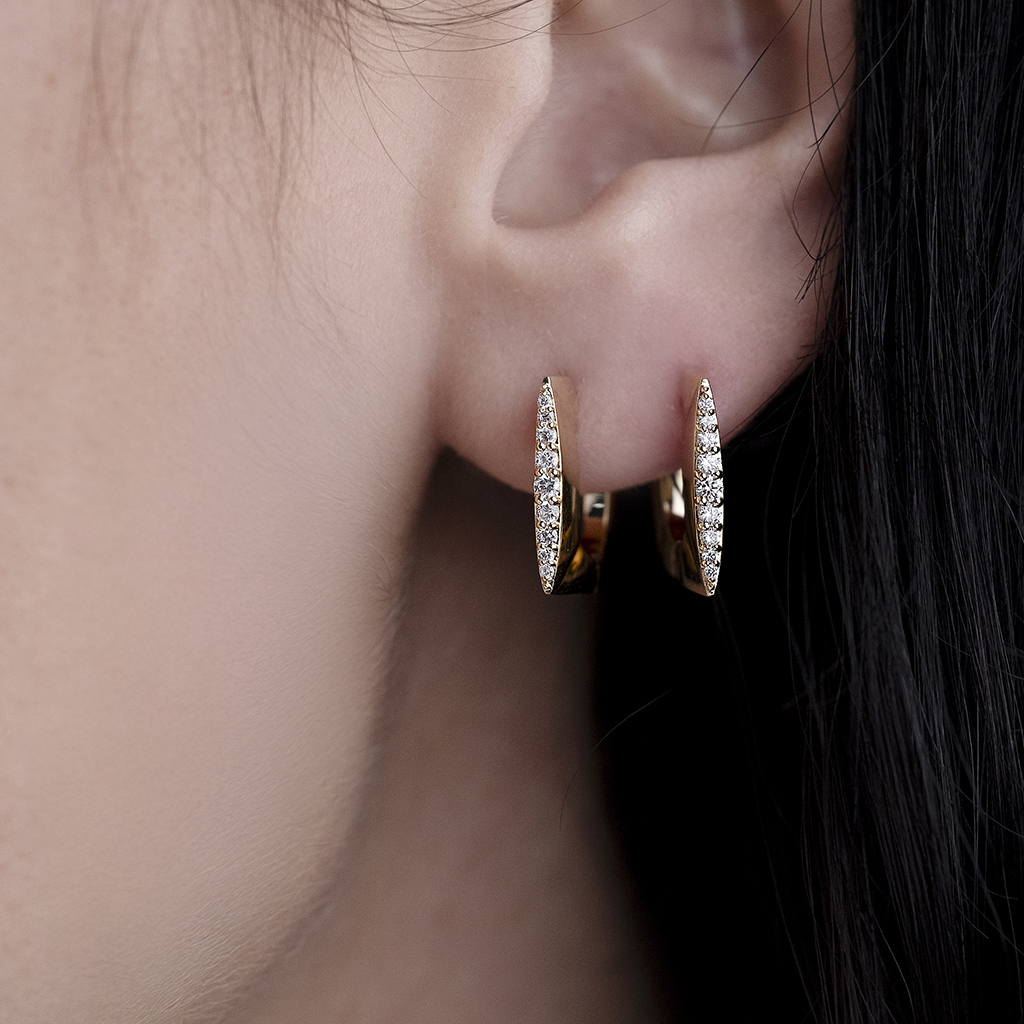 Close-up of gold hoop earrings featuring diamond accents worn on a person's ear.