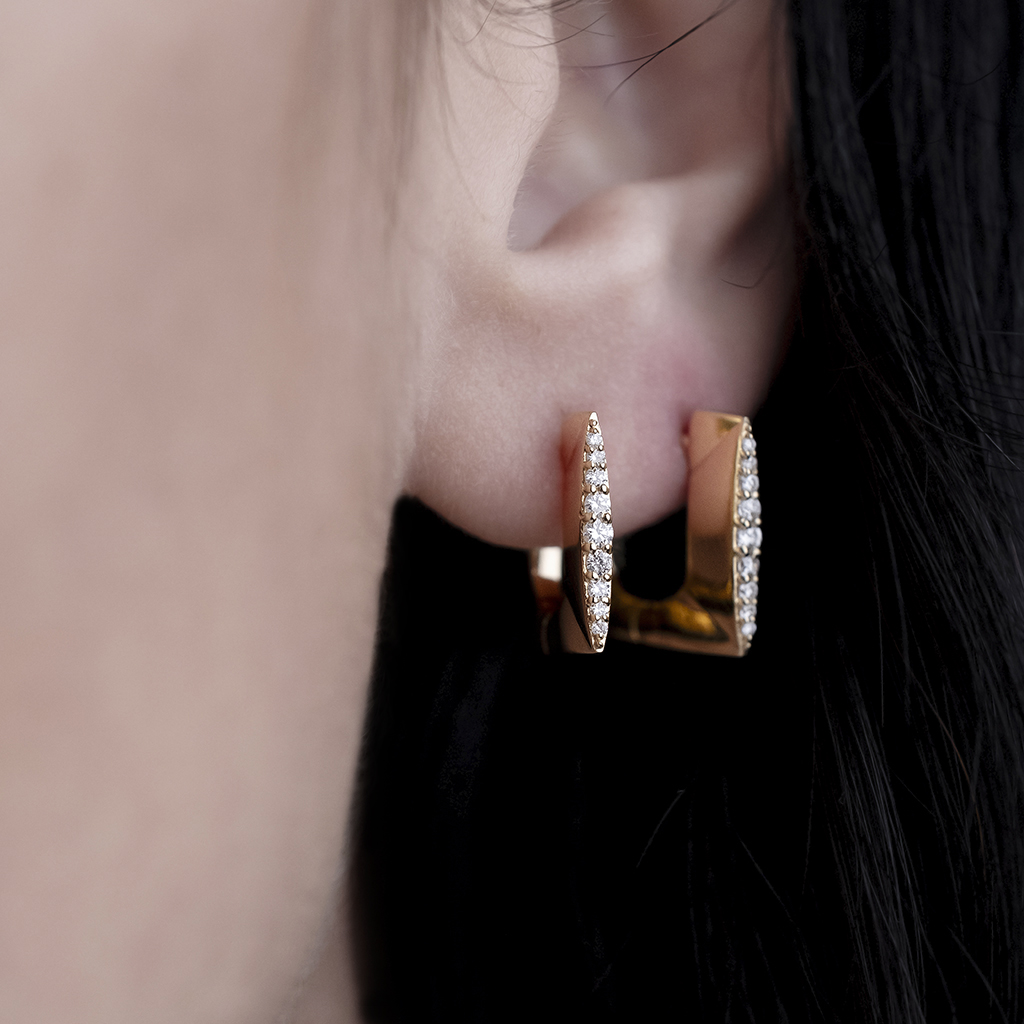 Close-up of a person's ear wearing gold earrings with diamond accents.
