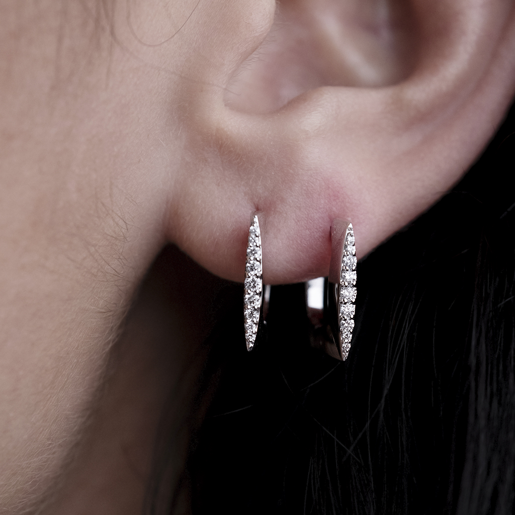 Close-up of silver hoop earrings featuring diamond accents worn on a person's ear.