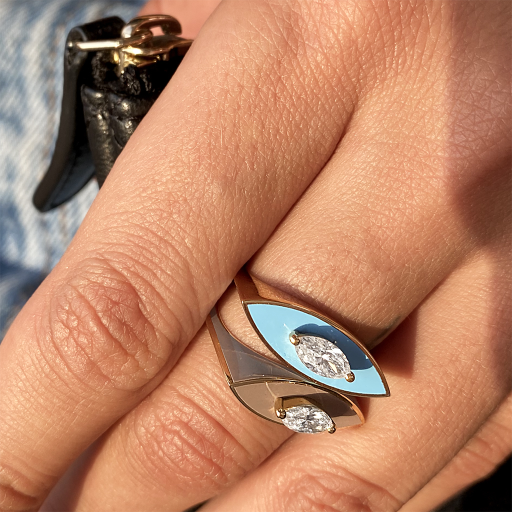 A close-up of a two-tone ring featuring an eye design with blue enamel and two gemstones.
